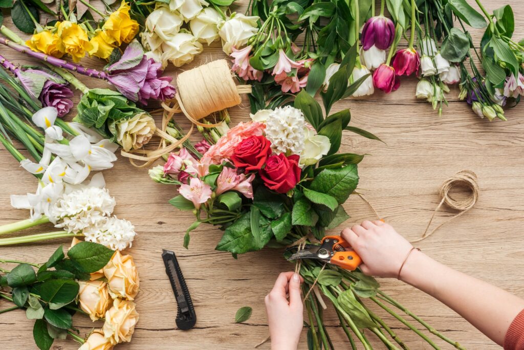 Cropped view of florist making flower bouquet on wooden surface